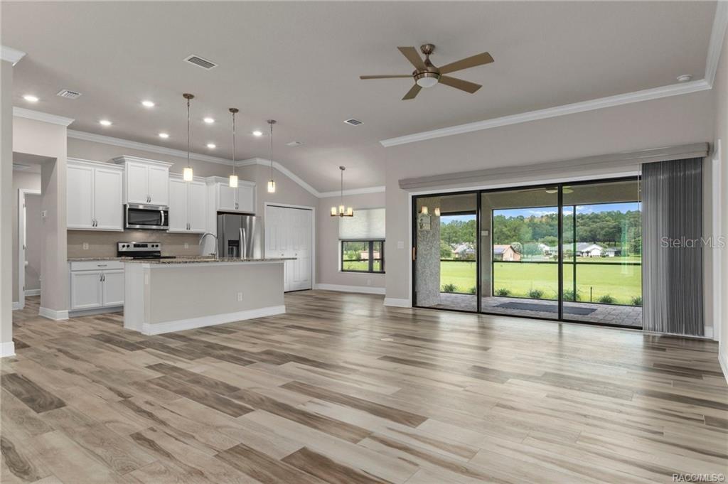 An open-concept kitchen and living area with white cabinets, wood-look flooring, and sliding glass doors — 295 E CUMBERLAND COURT, HERNANDO, FL