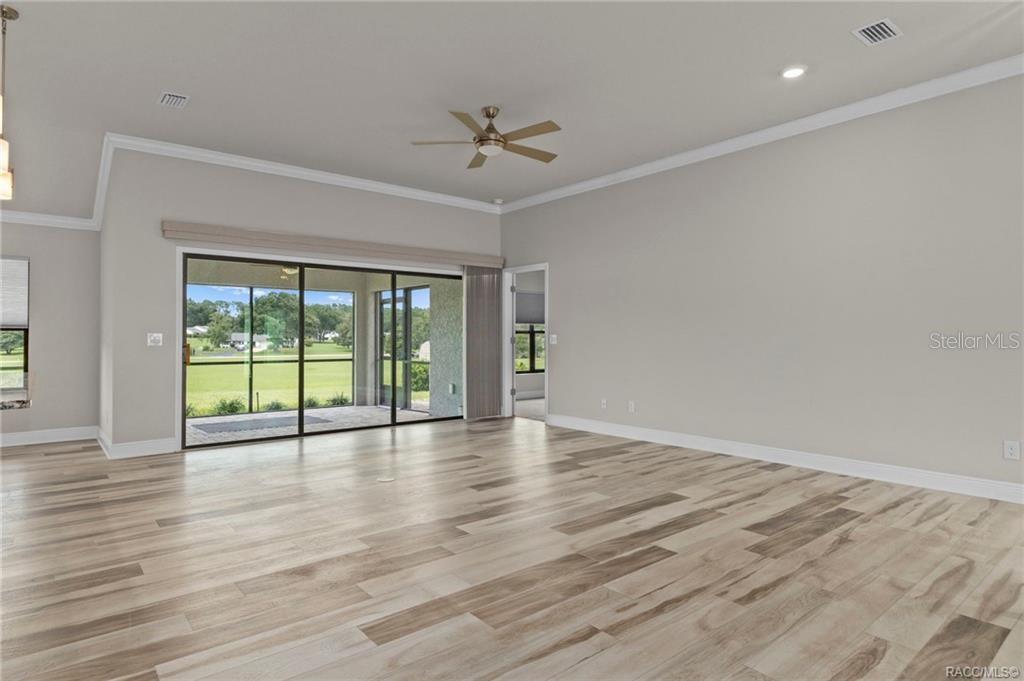 A spacious living room features light wood-look flooring, a ceiling fan, and large sliding glass doors — 295 E CUMBERLAND COURT, HERNANDO, FL