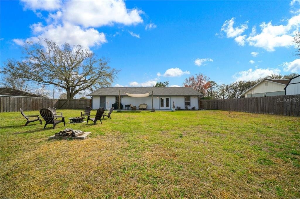 A backyard with a fire pit, patio furniture, and a white house under a blue sky — 685 NW 67TH PLACE, OCALA, FL