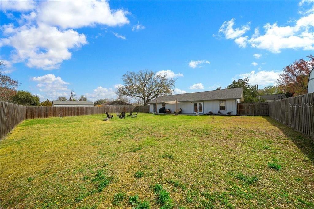 A large, fenced-in backyard features a grassy lawn, a patio, and a single-story house — 685 NW 67TH PLACE, OCALA, FL