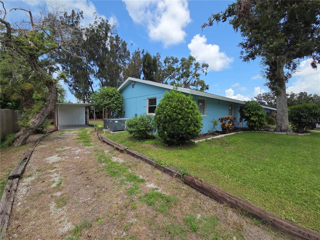 A light blue house with a gravel driveway and a detached carport under a blue sky — 4136 S LOCKWOOD RIDGE ROAD, SARASOTA, FL
