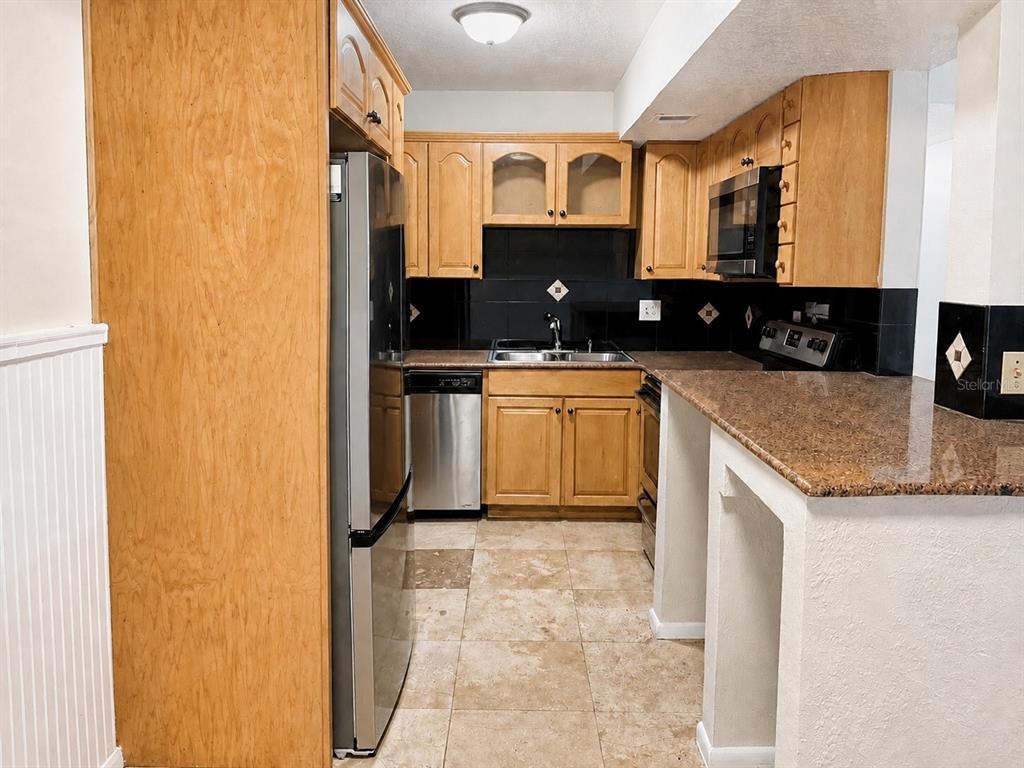 A kitchen features light wood cabinets, stainless steel appliances, dark countertops, and a tiled floor — 914 LAKE DESTINY ROAD UNIT F, ALTAMONTE SPRINGS, FL