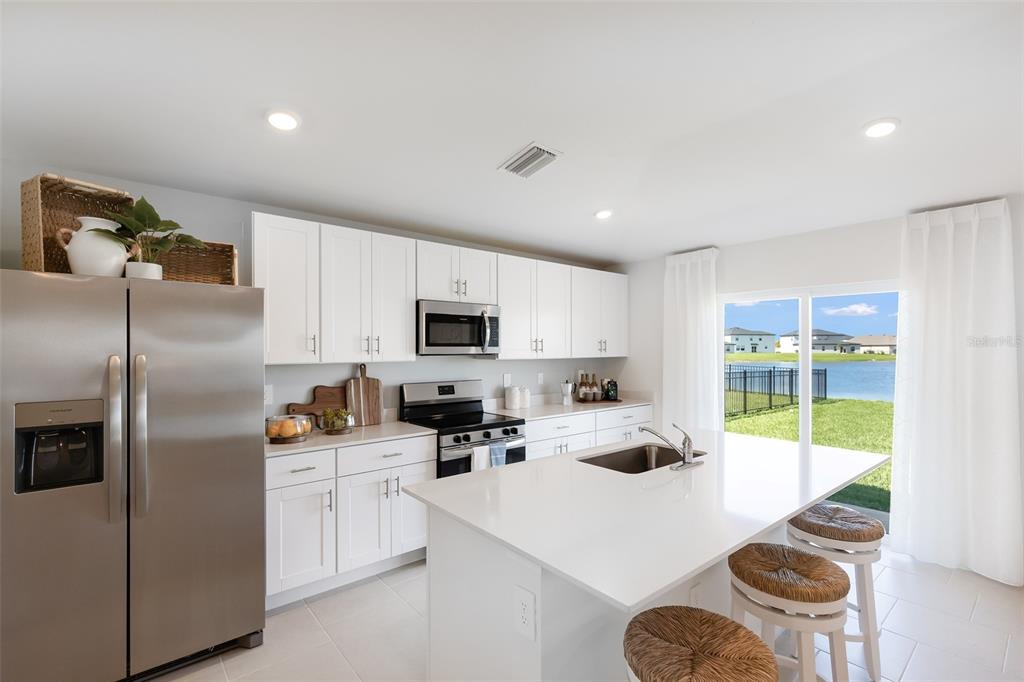 A modern kitchen features white cabinets, stainless steel appliances, a quartz island, and water views — 12077 BEIMAN AVENUE, PORT CHARLOTTE, FL