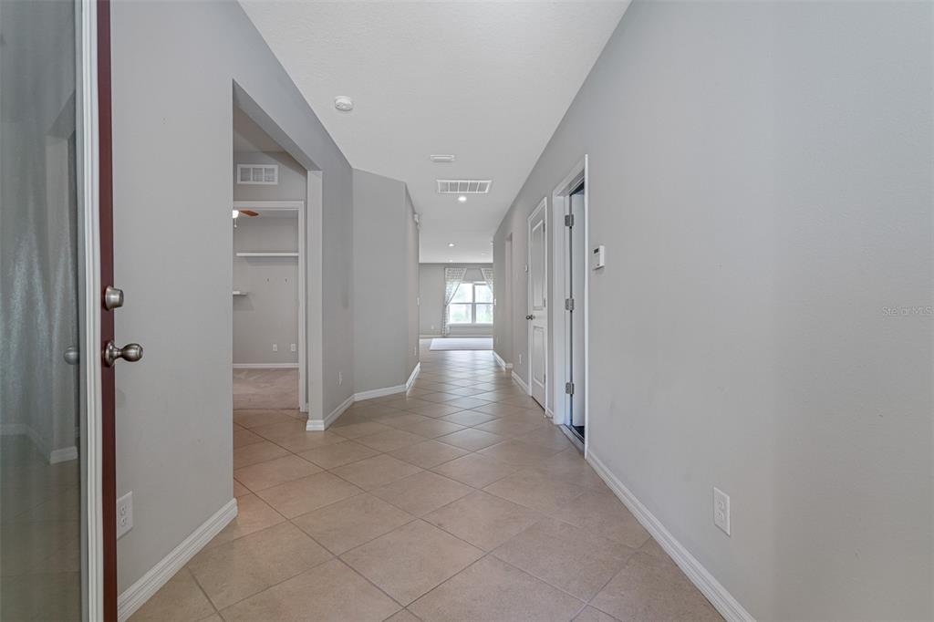 A tiled hallway leads from an entryway toward a bright room with a window — 11234 HIGH NOON TRAIL, PARRISH, FL