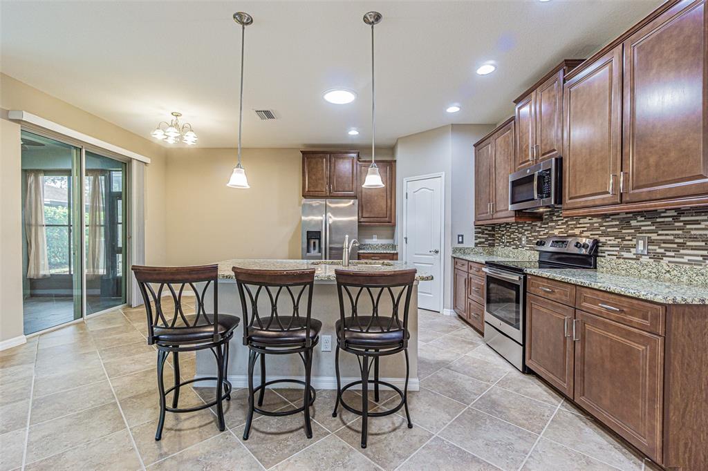 A kitchen features dark wood cabinets, granite countertops, stainless steel appliances, and a breakfast bar — 9936 GAP WEDGE DRIVE, SAN ANTONIO, FL