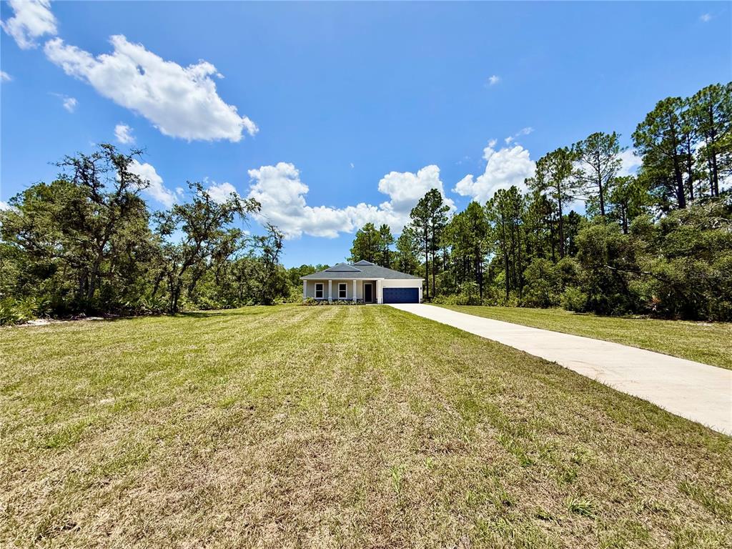 A single-story house with a concrete driveway sits on a large, grassy lot — 30280 W BLUEBELL AVENUE, EUSTIS, FL