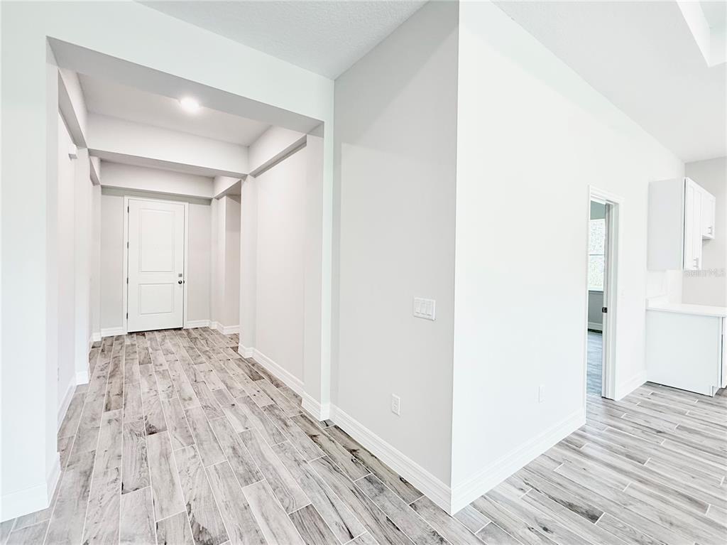 A hallway with wood-look tile flooring leads to a white door near a kitchen — 30280 W BLUEBELL AVENUE, EUSTIS, FL