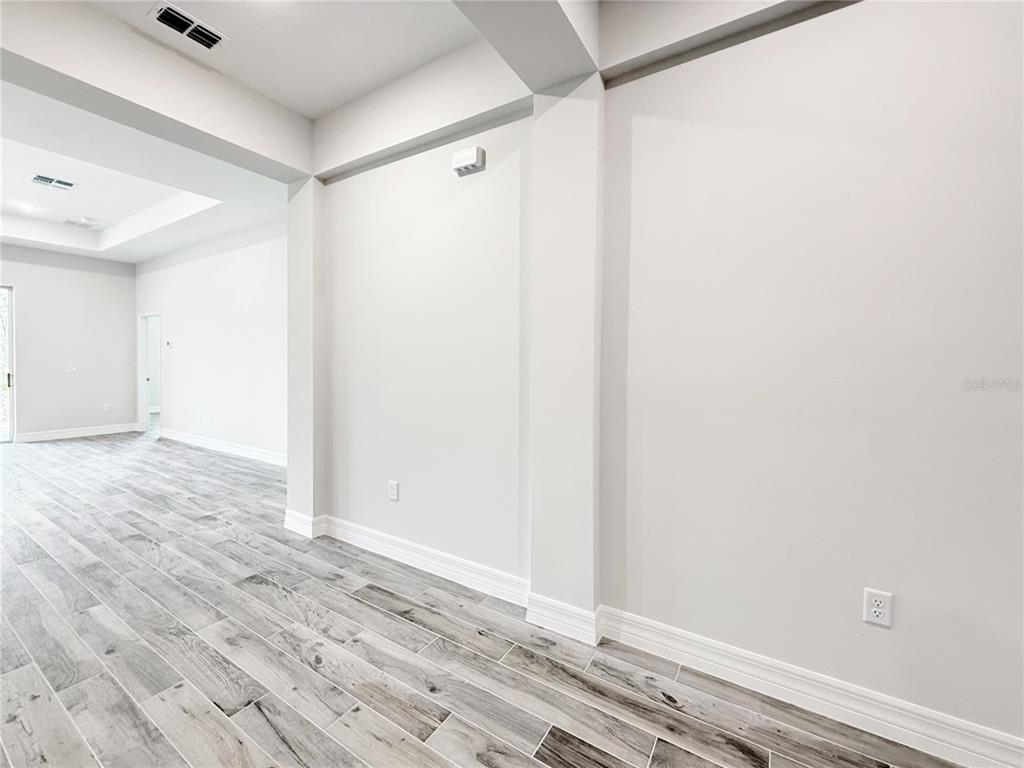 A bright, empty room features light gray wood-look tile flooring and white walls — 30280 W BLUEBELL AVENUE, EUSTIS, FL