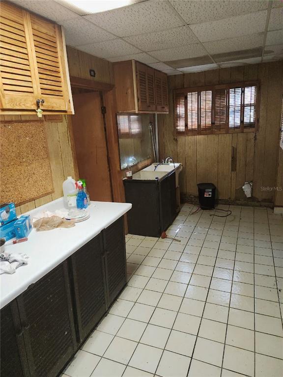 A kitchen features wood-paneled walls, louvered cabinets, a white countertop, and a tiled floor — 610 TANGLEWOOD STREET, DAYTONA BEACH, FL