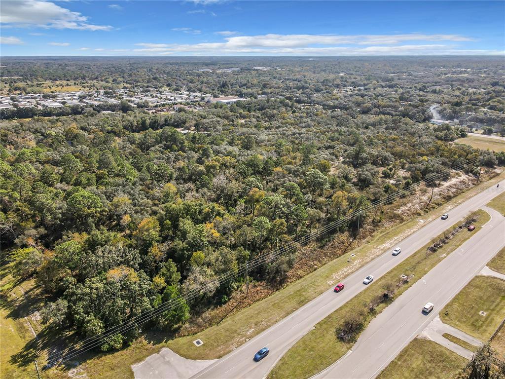 An aerial view shows a large, wooded plot of land adjacent to a multi-lane highway — 0000 LITTLE, HUDSON, FL