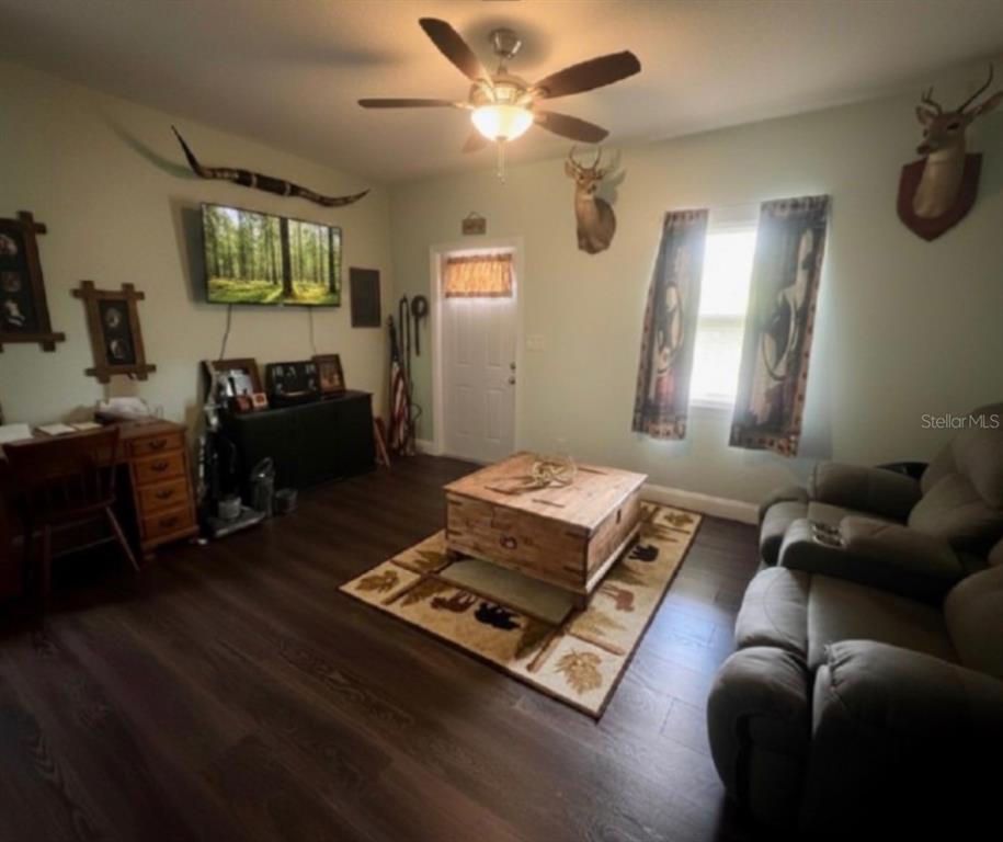 A living room features wood-look flooring, a ceiling fan, a coffee table, and taxidermy decor — 117 S MANATEE AVENUE, ARCADIA, FL