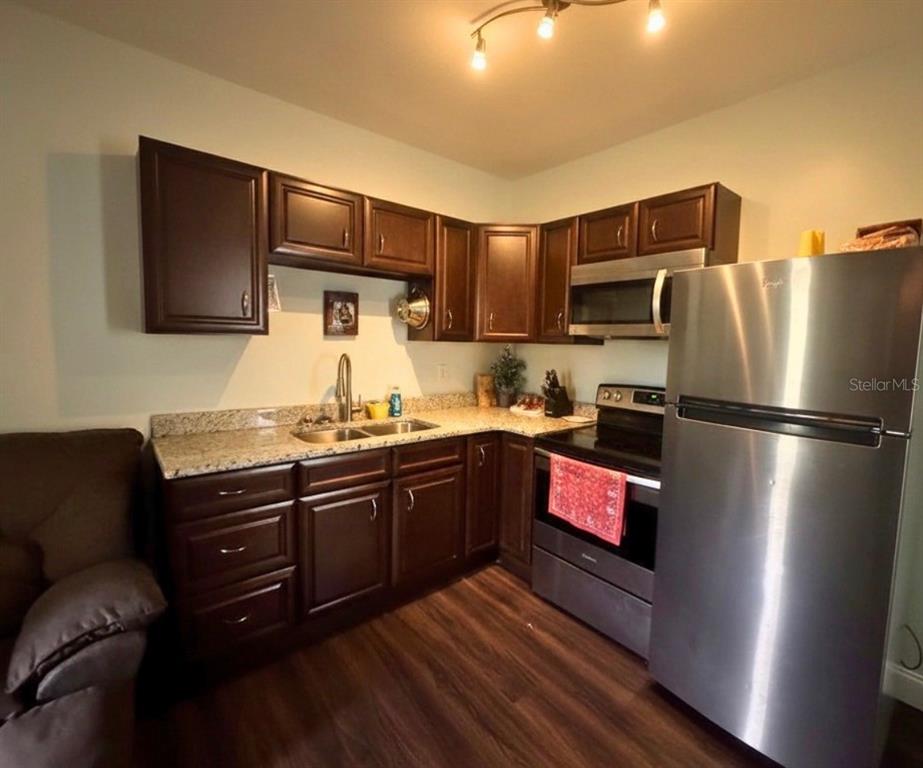 A kitchen features dark wood cabinets, granite countertops, stainless steel appliances, and wood-look flooring — 117 S MANATEE AVENUE, ARCADIA, FL