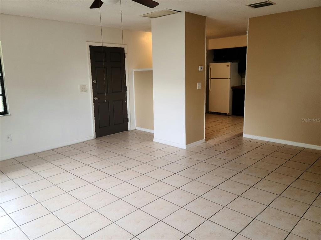 An open-concept living area with light-colored floor tiles, a dark entry door, and a kitchen — 2712 TORTOISE CV, WINTER PARK, FL