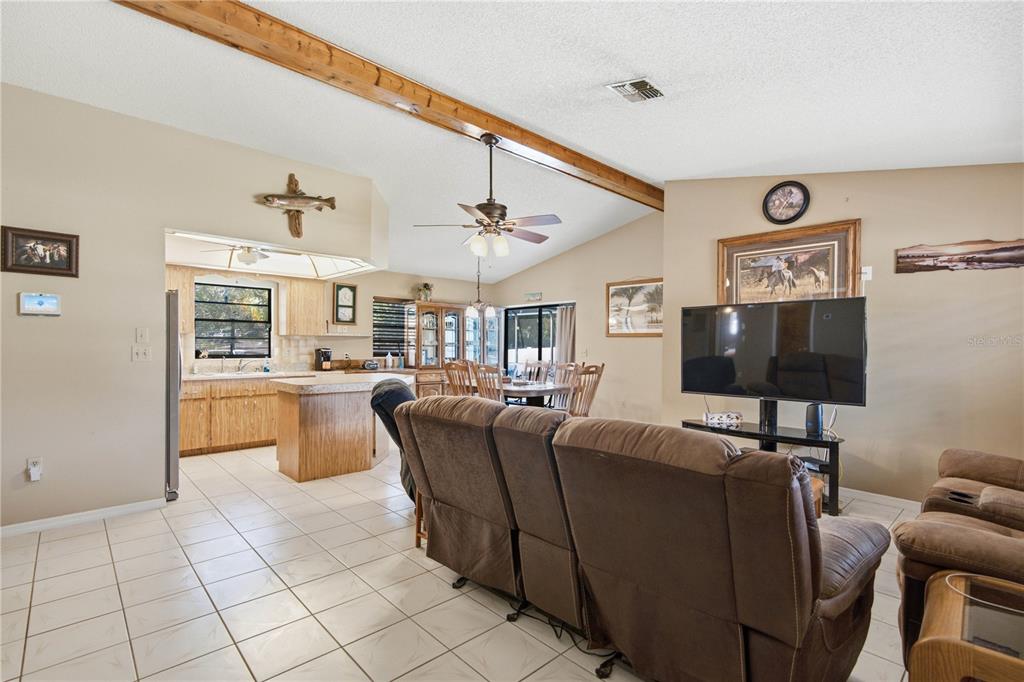 An open-concept living room and kitchen feature tile flooring, wooden ceiling beams, and brown furniture — 11423 LINDEN DRIVE, SPRING HILL, FL