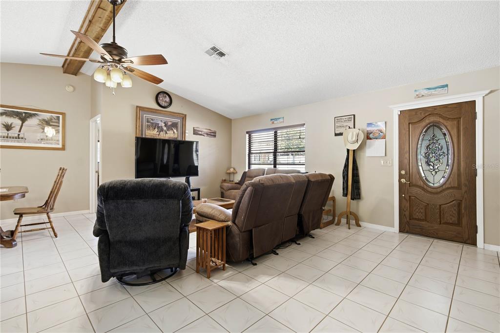 A living room features tile flooring, a ceiling fan, a television, and a wooden front door — 11423 LINDEN DRIVE, SPRING HILL, FL