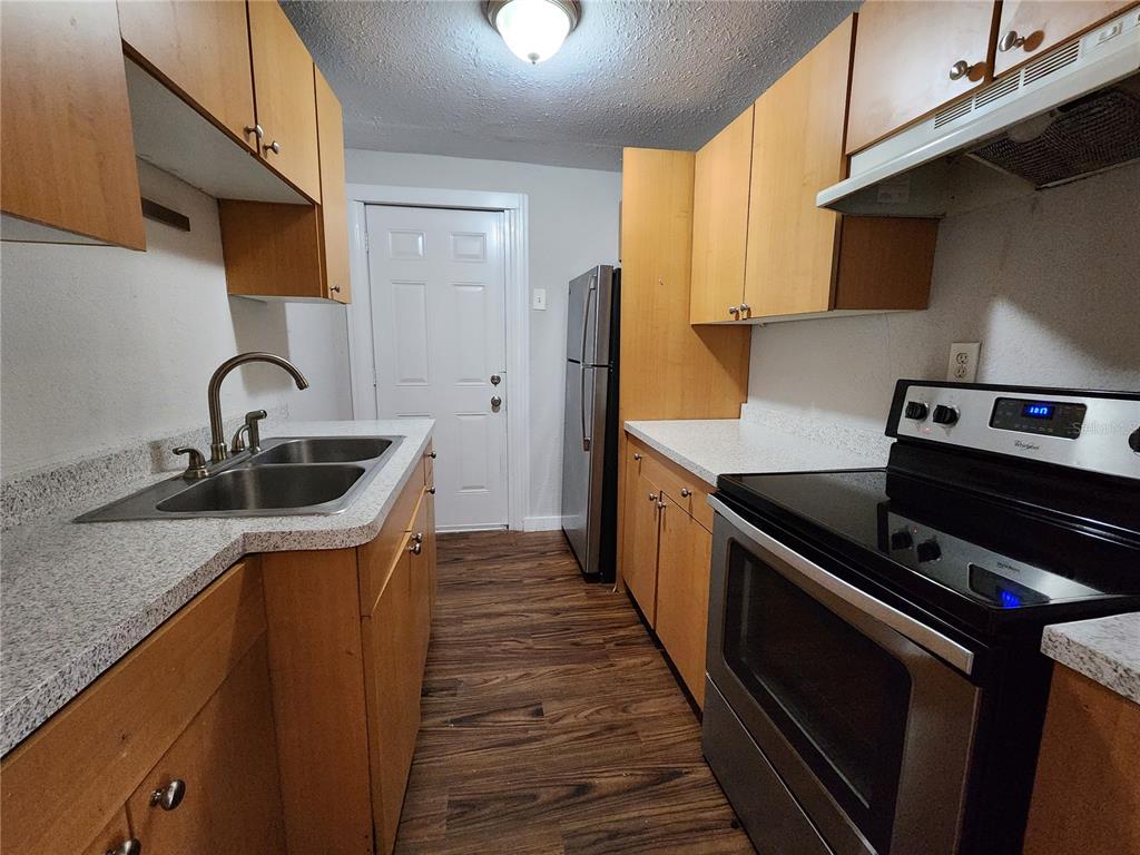A galley kitchen features light wood cabinets, speckled countertops, stainless steel appliances, and wood flooring — 2110 W 41ST STREET, JACKSONVILLE, FL