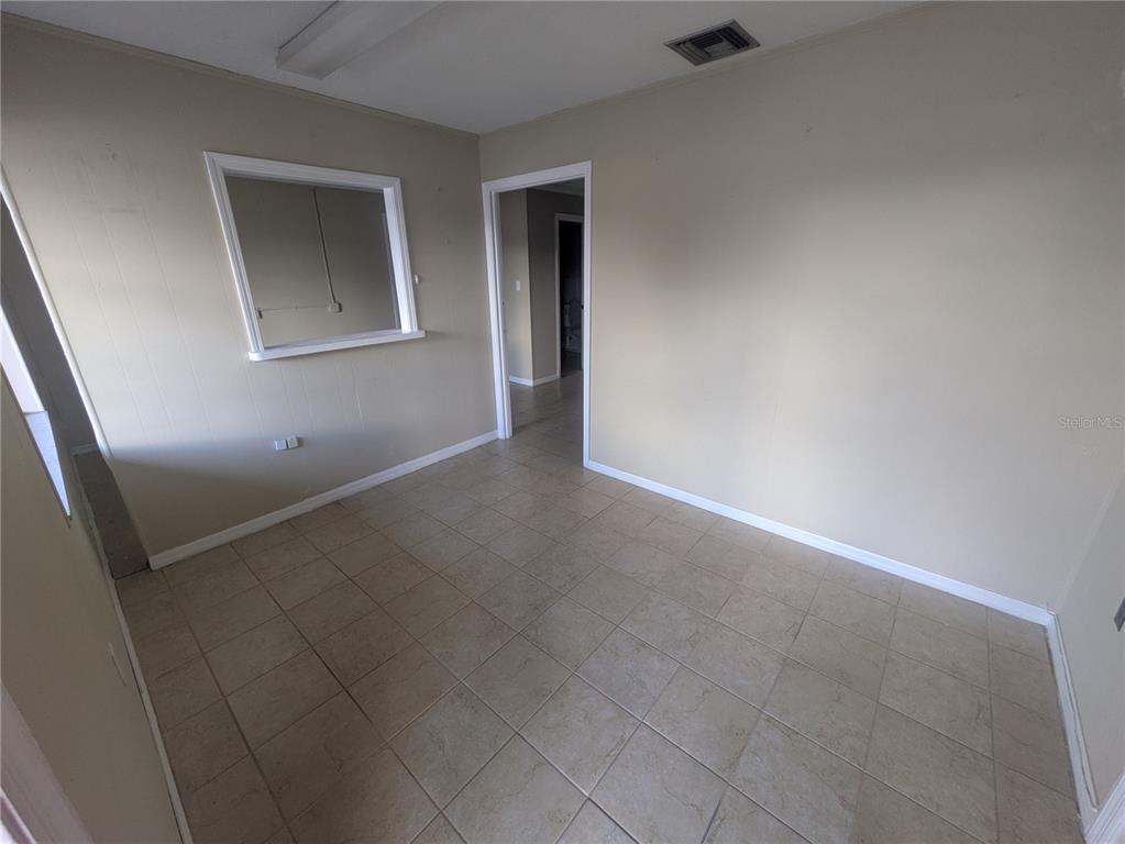 An empty room features beige walls, light-colored tile flooring, a pass-through window, and a doorway — 247 W MAIN STREET, APOPKA, FL