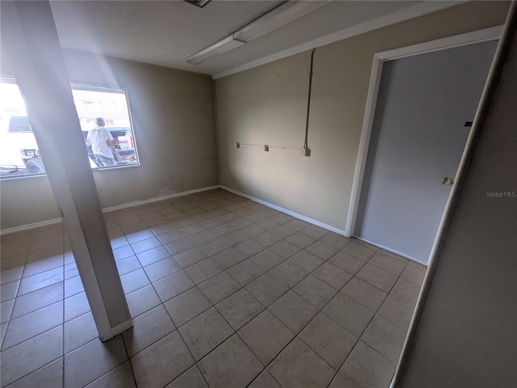An empty room features beige walls, tiled flooring, a window, and an exposed electrical conduit — 247 W MAIN STREET, APOPKA, FL