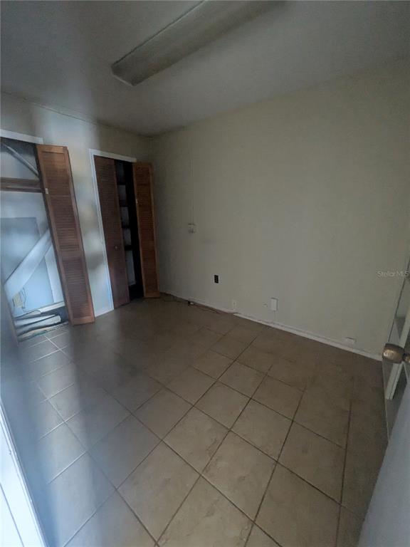 An empty room with beige tile flooring, plain walls, and wooden louvered closet doors — 247 W MAIN STREET, APOPKA, FL