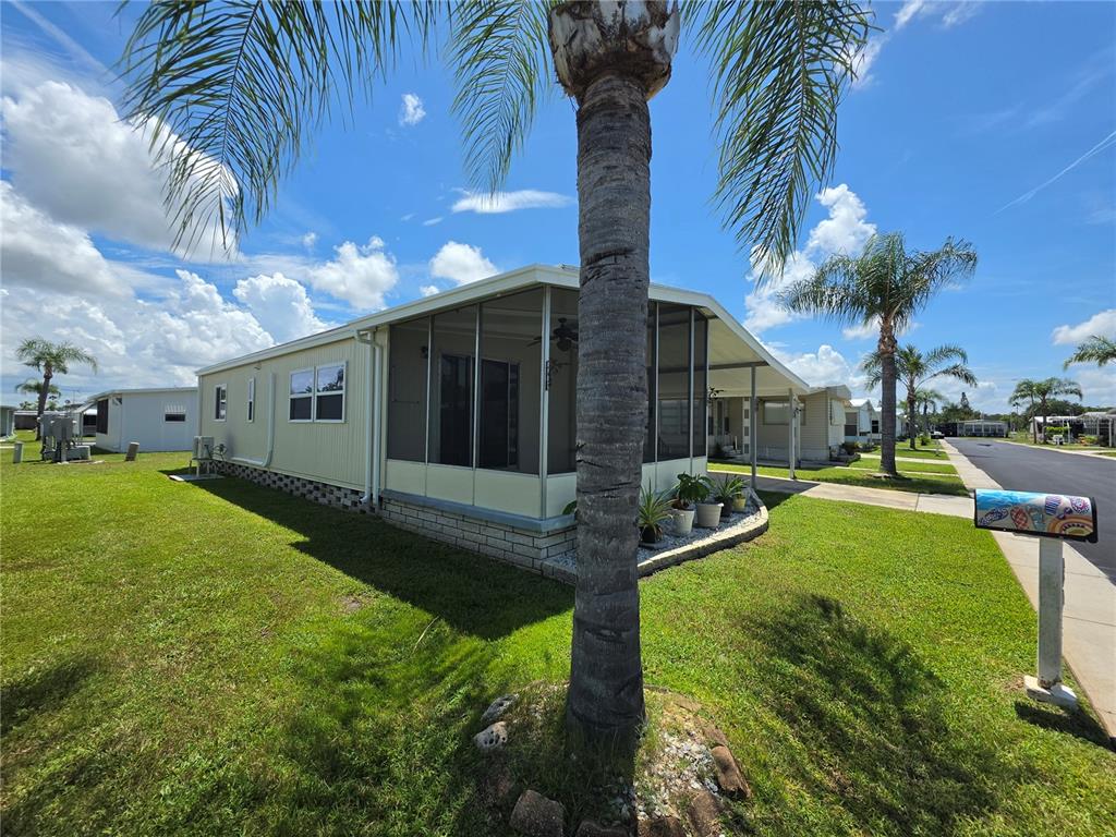 A light-colored mobile home features a screened-in porch and a palm tree in the yard — 10924 HERITAGE DRIVE, PORT RICHEY, FL