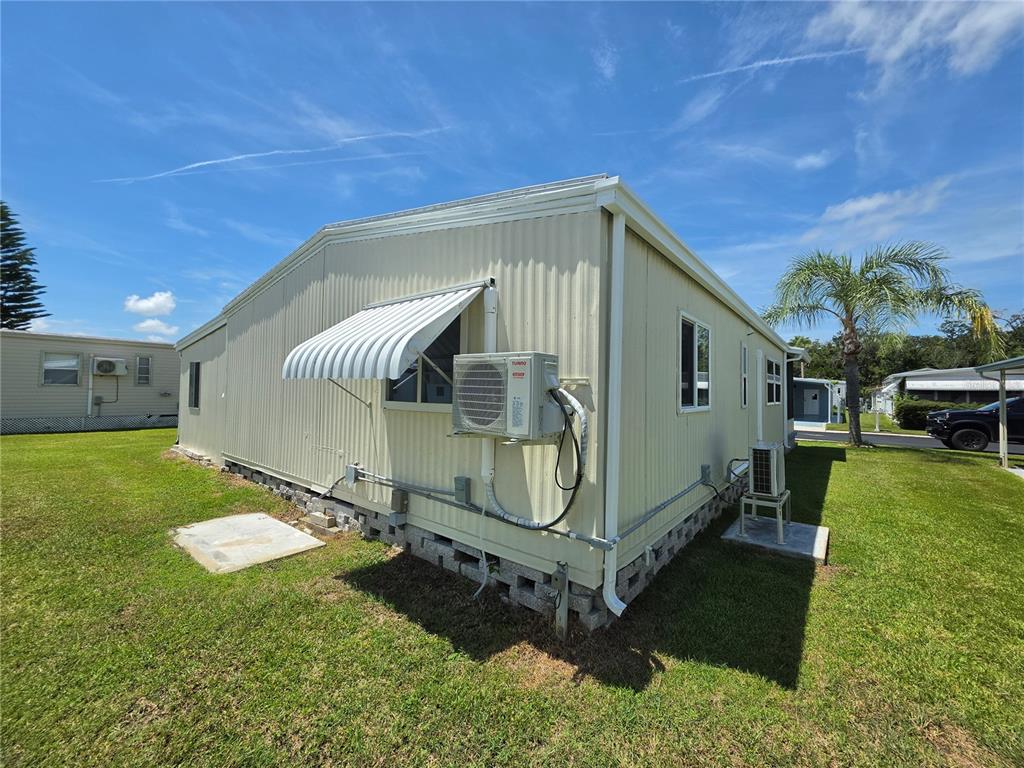 The exterior of a light-colored mobile home features a wall-mounted air conditioning unit and awning — 10924 HERITAGE DRIVE, PORT RICHEY, FL