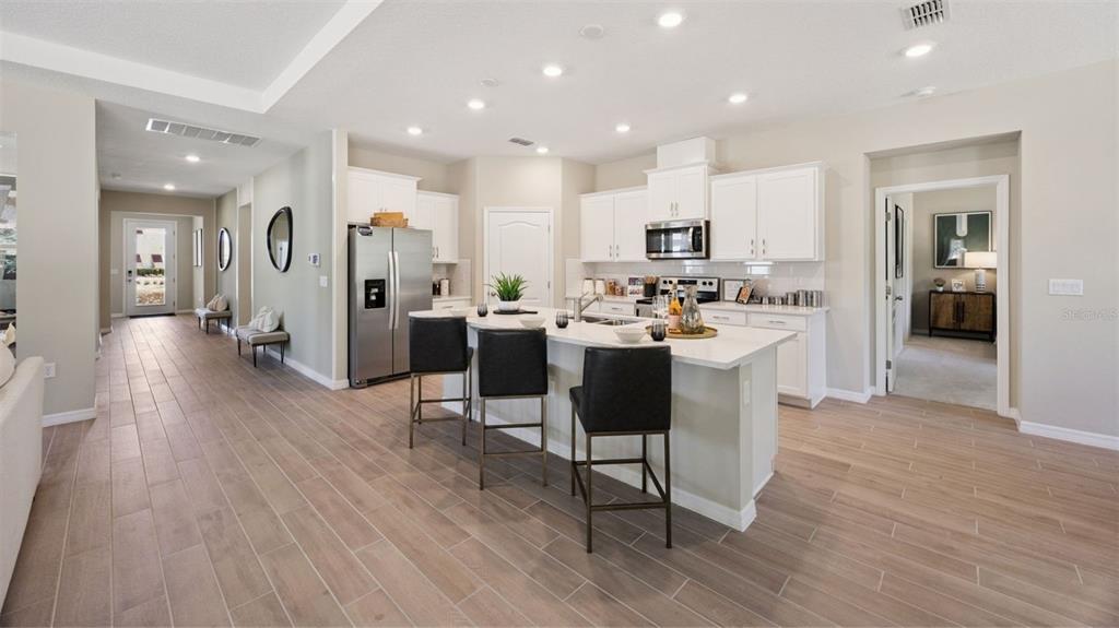 A modern kitchen features white cabinets, a central island with three stools, and tile flooring — 3050 KINGSMAN TRAIL, ORMOND BEACH, FL