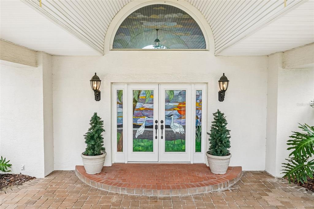 An exterior view of a front entryway featuring double doors with stained glass heron panels — 5198 LEGEND HILLS LANE, SPRING HILL, FL