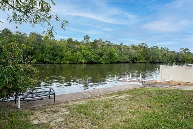 A grassy backyard features a concrete seawall, a metal bench, and a private boat dock — 6807 EDGEWATER DRIVE, NEW PORT RICHEY, FL