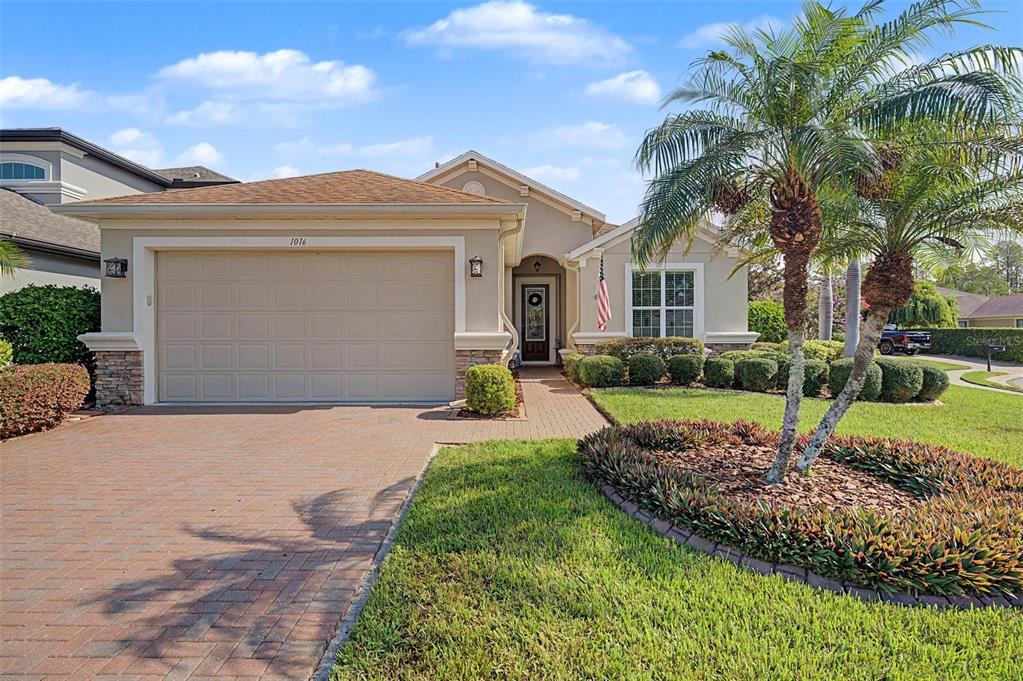 A single-story house with a tan exterior, brick driveway, and a palm tree in front — 1016 KETZAL DRIVE, TRINITY, FL