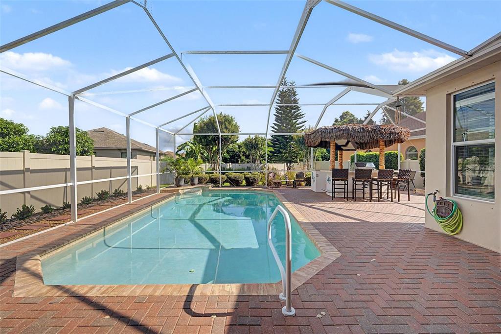 A swimming pool with a screened enclosure and a tiki bar on a brick patio — 1016 KETZAL DRIVE, TRINITY, FL