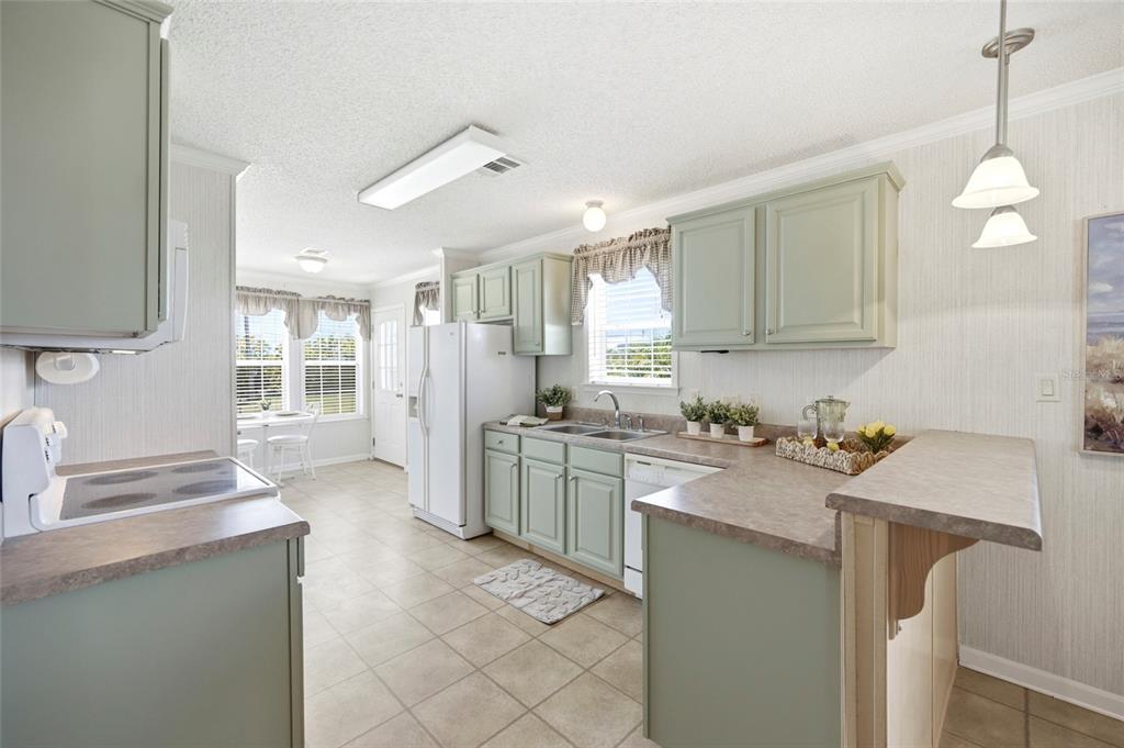A kitchen with sage green cabinets, laminate countertops, white appliances, and a breakfast bar — 2 HOLLAND DRIVE UNIT 39E, PUNTA GORDA, FL