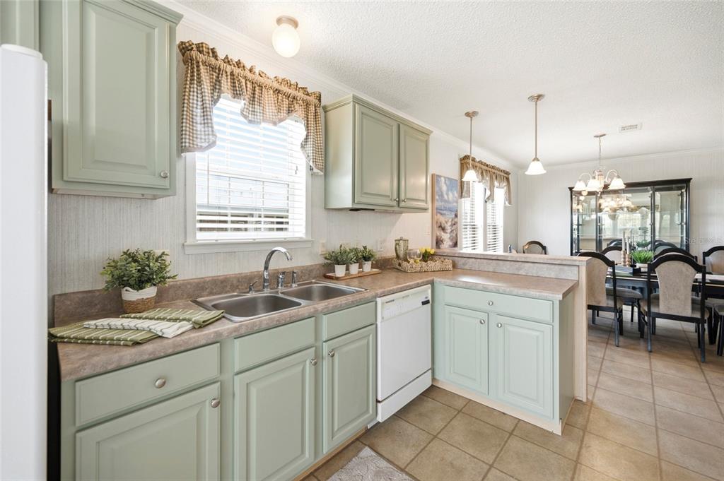 A kitchen with light green cabinets, laminate countertops, and an adjacent dining area — 2 HOLLAND DRIVE UNIT 39E, PUNTA GORDA, FL