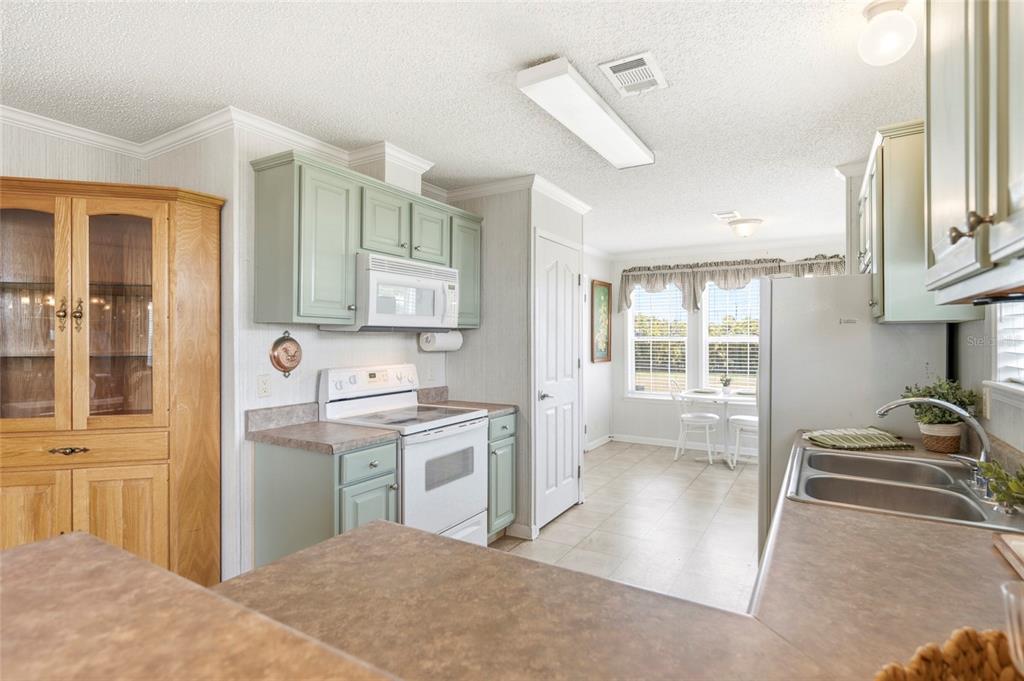 A kitchen features light green cabinets, white appliances, a wood hutch, and an adjacent dining area — 2 HOLLAND DRIVE UNIT 39E, PUNTA GORDA, FL
