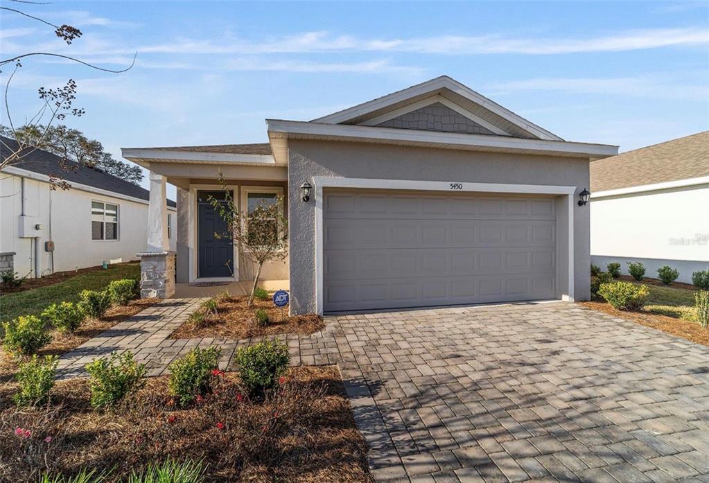 A single-story house with a beige stucco exterior, a gray garage door, and a paver driveway — 5450 NW 46TH LANE ROAD, OCALA, FL