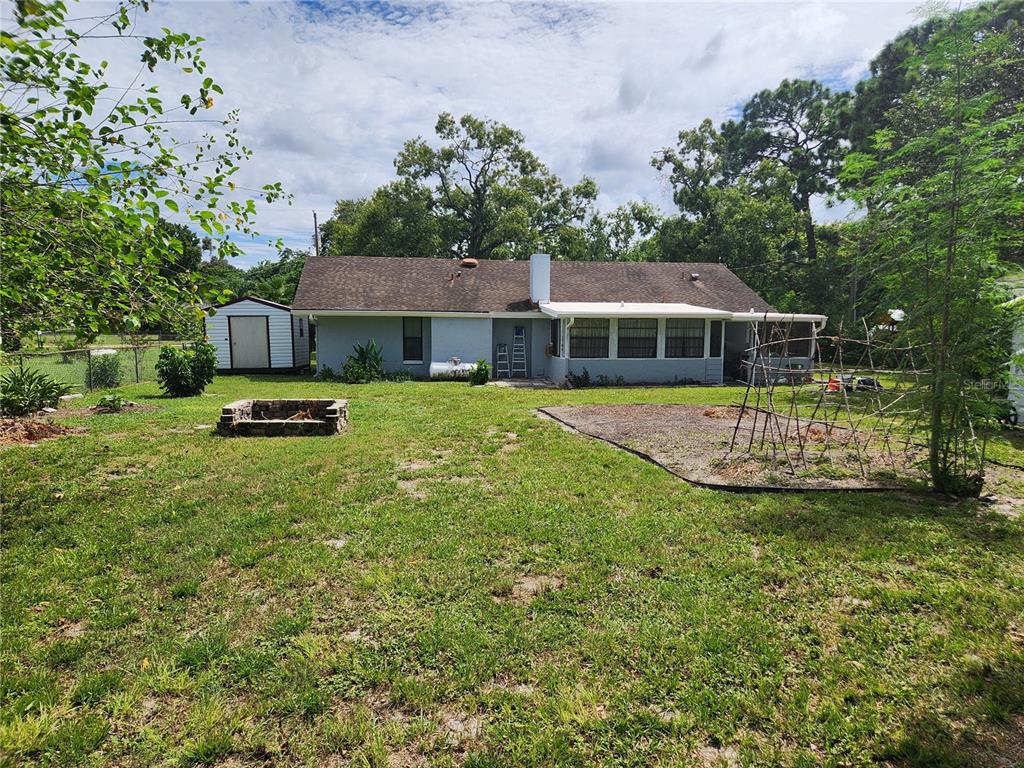 The backyard of a single-story house features a fire pit, garden bed, and storage shed — 9511 CLYDE STREET, HUDSON, FL