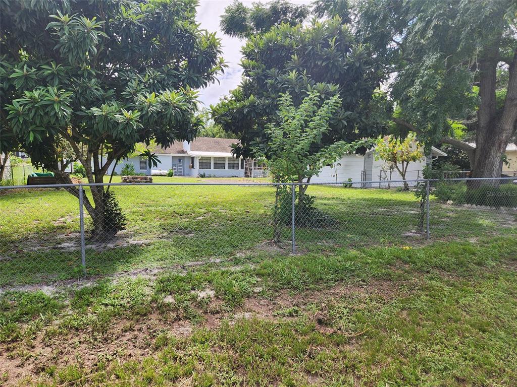 A chain-link fence separates a grassy backyard from a light-colored house with mature trees — 9511 CLYDE STREET, HUDSON, FL