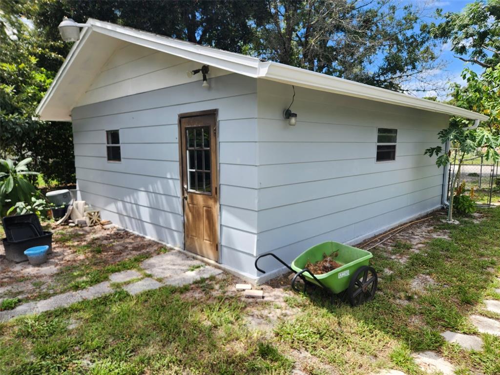 The exterior of a light blue detached garage with a wooden door and a wheelbarrow — 9511 CLYDE STREET, HUDSON, FL