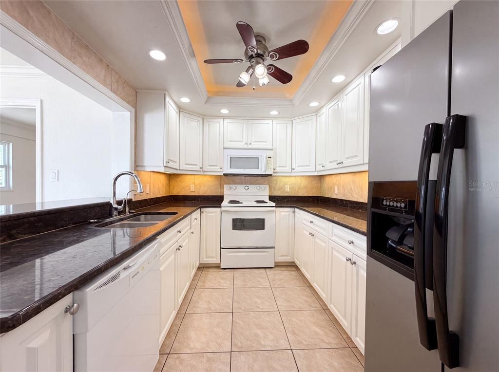 A kitchen features white cabinets, dark countertops, white appliances, and a ceiling fan — 1672 JUPITER ROAD, VENICE, FL