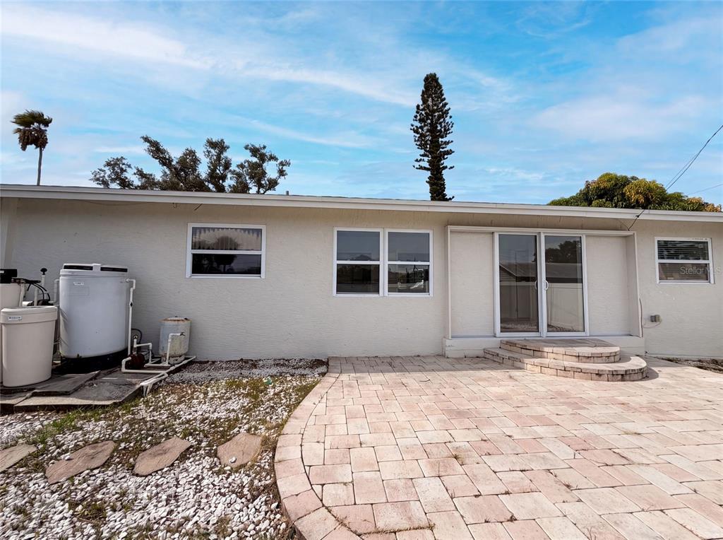 The exterior of a house features a paved patio, sliding glass doors, and water equipment — 1672 JUPITER ROAD, VENICE, FL