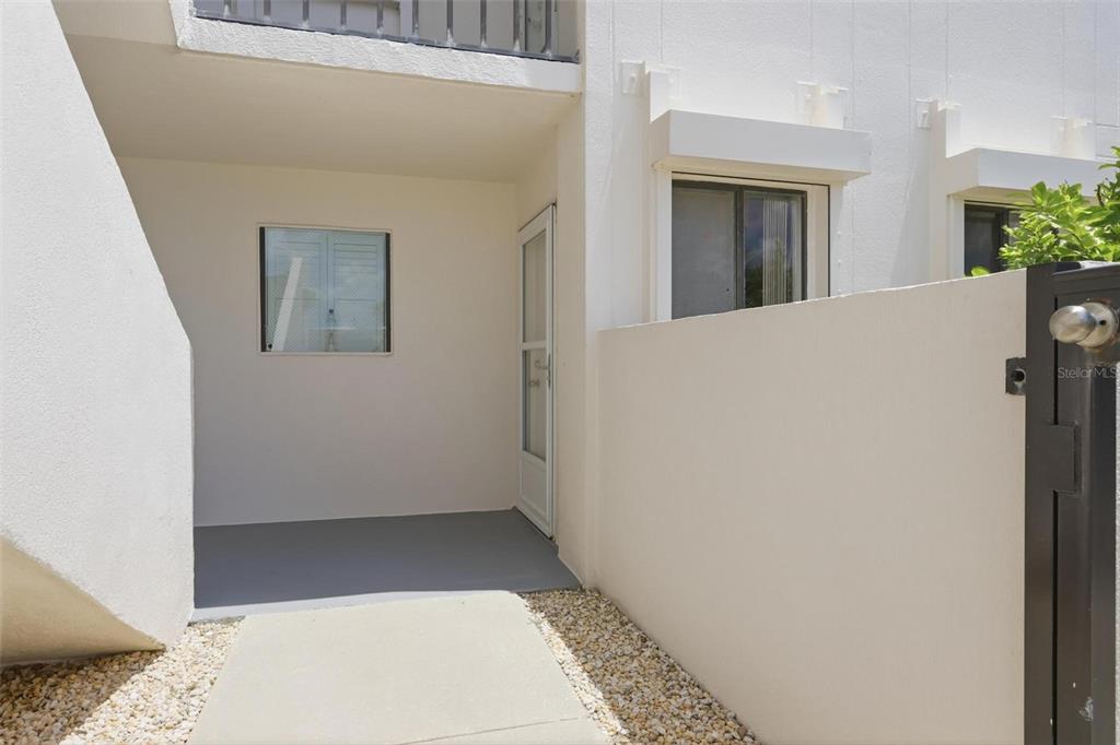 A white exterior entryway features a concrete walkway, a screen door, and a privacy wall — 2860 OCEAN SHORE BOULEVARD UNIT 1010, ORMOND BY THE SEA, FL