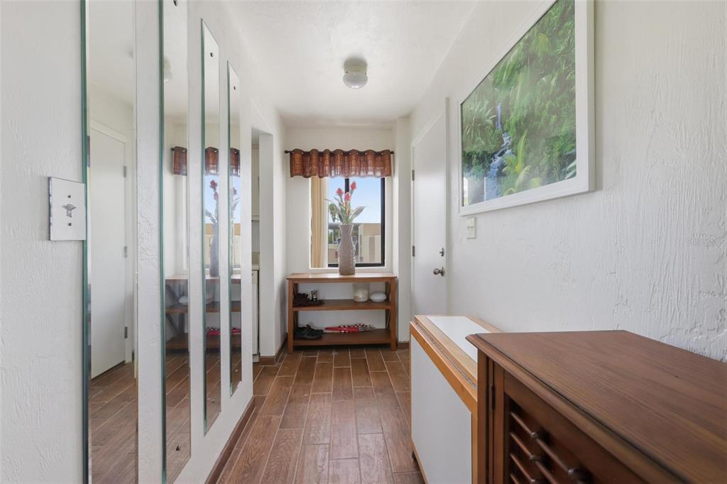 A hallway features wood-look tile flooring, mirrored wall panels, and a wooden console table — 2860 OCEAN SHORE BOULEVARD UNIT 1010, ORMOND BY THE SEA, FL