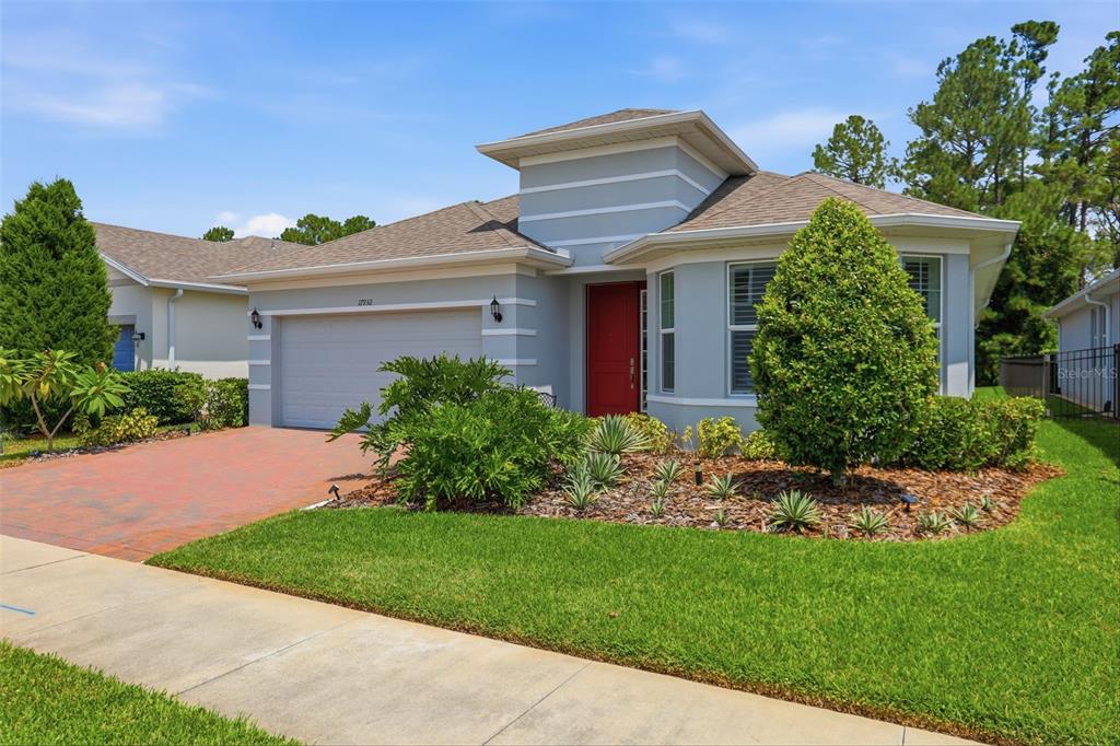 A single-story house with a grey exterior, red front door, and a brick paver driveway — 17932 PASSIONFLOWER CIRCLE, CLERMONT, FL