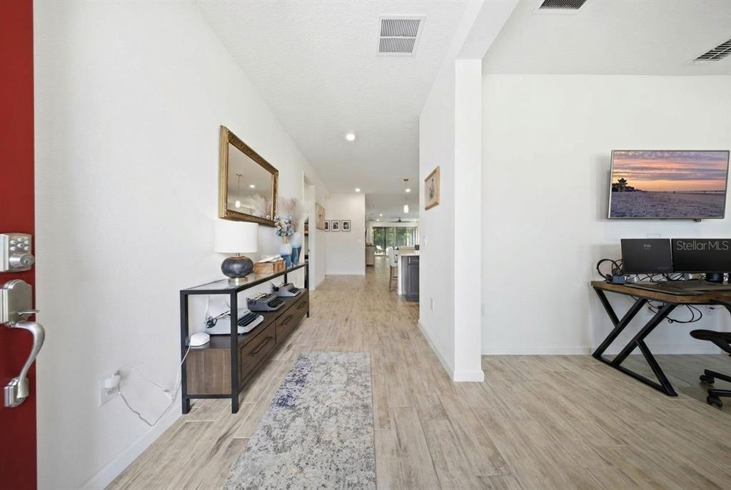 An entryway with wood-look tile flooring leads into an open-concept home with a desk area — 17932 PASSIONFLOWER CIRCLE, CLERMONT, FL