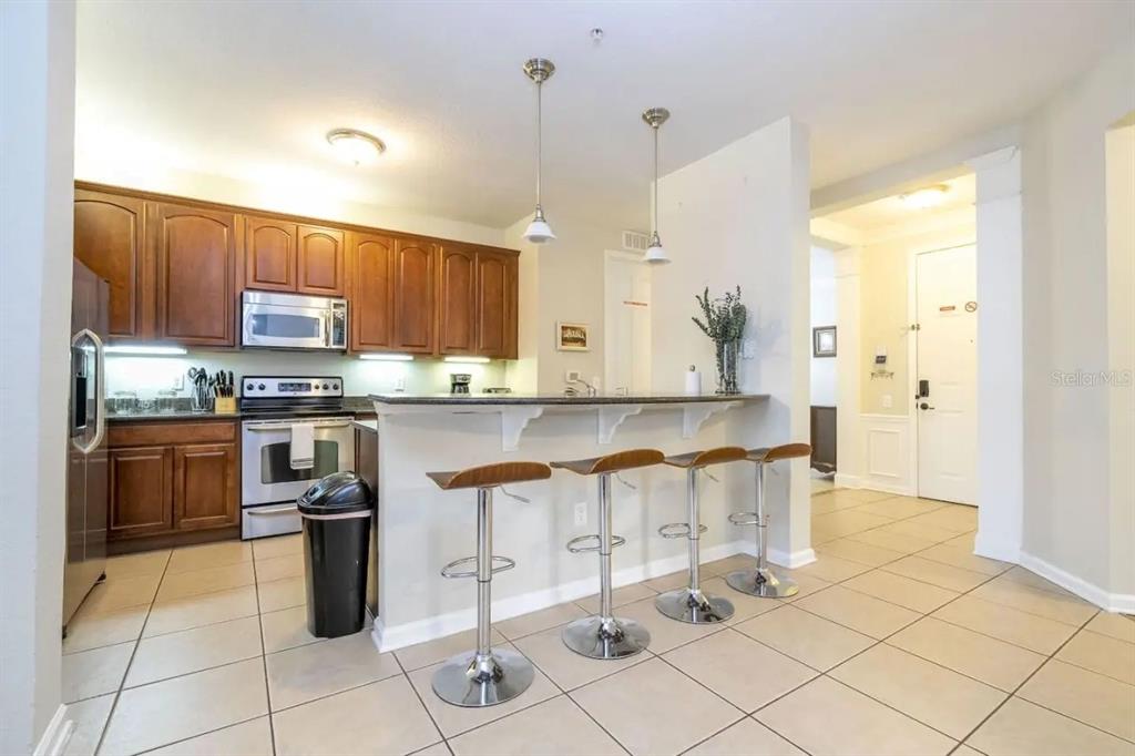 A kitchen with wood cabinets, stainless steel appliances, and a breakfast bar with four stools — 5025 SHOREWAY LOOP UNIT 10703, ORLANDO, FL