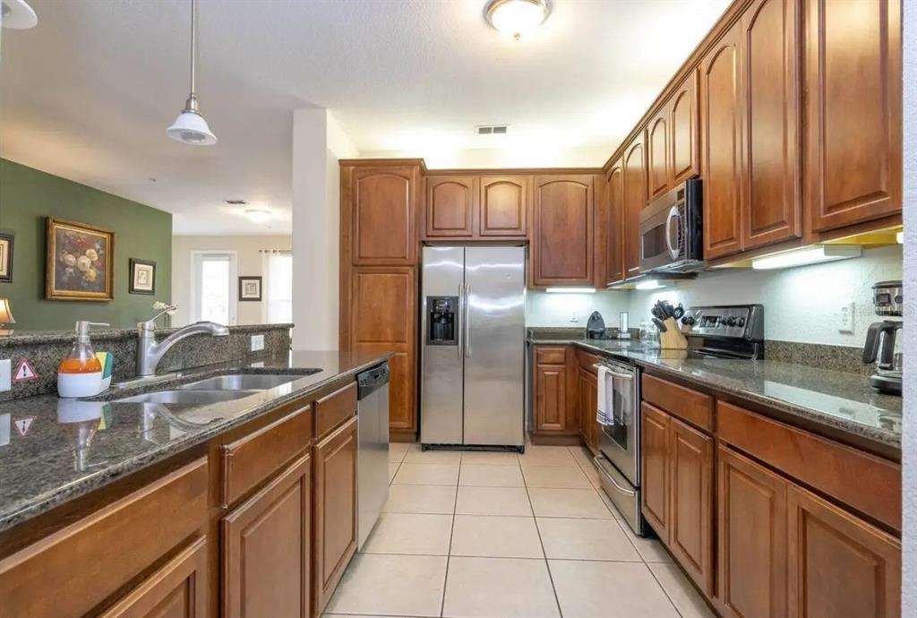 A kitchen features wood cabinets, granite countertops, stainless steel appliances, and tile flooring — 5025 SHOREWAY LOOP UNIT 10703, ORLANDO, FL