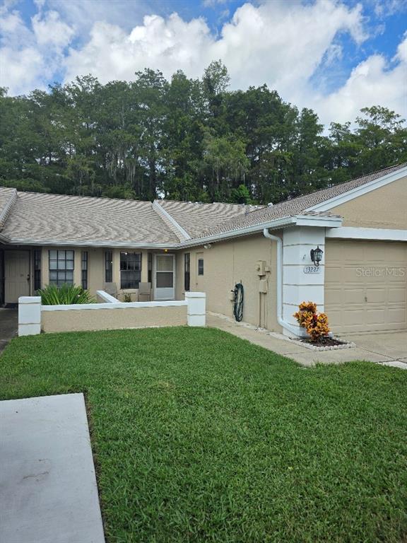 A tan single-story townhouse features a garage, a small front patio, and a grassy lawn — 13227 MOLITOR COURT, HUDSON, FL