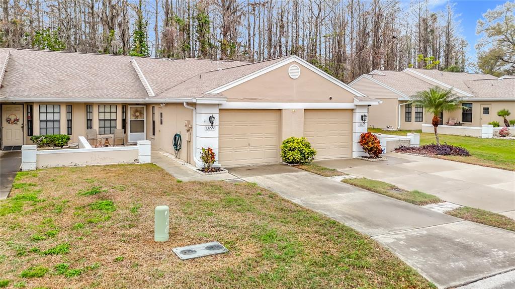 A single-story duplex with tan stucco walls, two garage doors, and a small front yard — 13227 MOLITOR COURT, HUDSON, FL