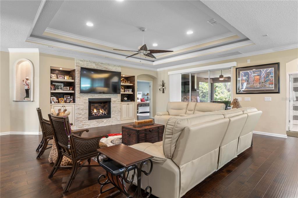 A living room with a stone fireplace, built-in shelving, hardwood floors, and a tray ceiling — 148 S COOPERS HAWK WAY, PALM COAST, FL