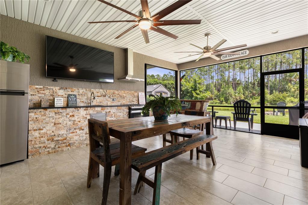 A covered outdoor patio features a stone-accented kitchen, dining table, and views of a pond — 148 S COOPERS HAWK WAY, PALM COAST, FL