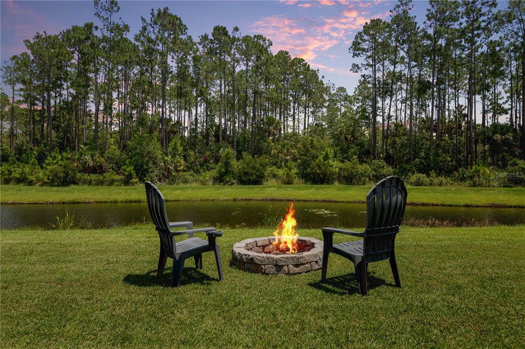 Two dark chairs sit on a grassy lawn beside a stone fire pit near water — 148 S COOPERS HAWK WAY, PALM COAST, FL